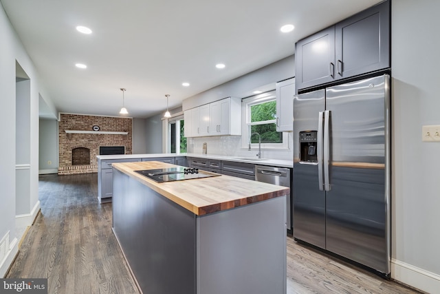 kitchen featuring a peninsula, wood finished floors, a sink, wood counters, and stainless steel appliances