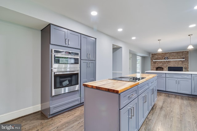 kitchen featuring butcher block countertops, black electric stovetop, gray cabinets, double oven, and light wood-style floors