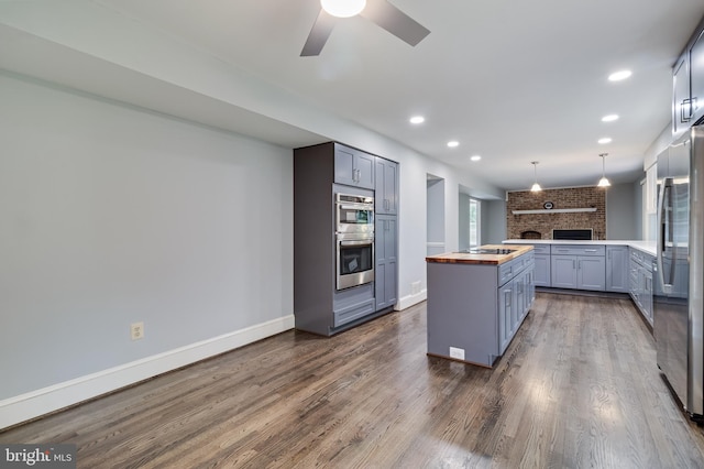 kitchen featuring stainless steel appliances, butcher block counters, dark wood-style flooring, a ceiling fan, and baseboards