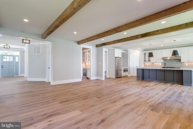 unfurnished living room with baseboards, light wood-type flooring, beam ceiling, and visible vents