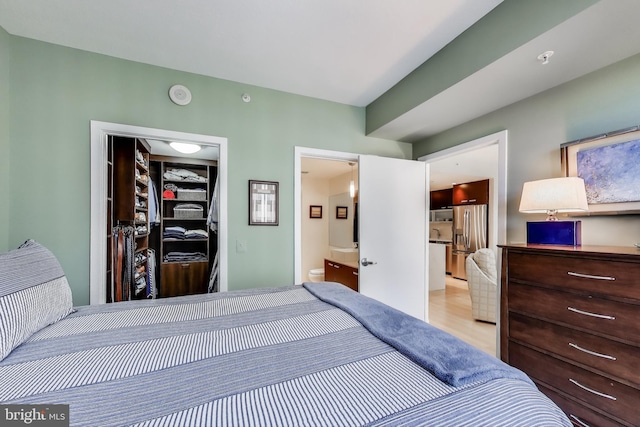 bedroom featuring a walk in closet, stainless steel refrigerator with ice dispenser, a closet, and connected bathroom