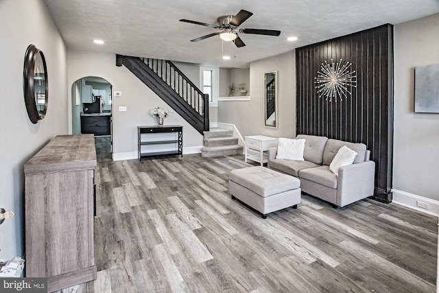 living room with stairs, baseboards, arched walkways, a ceiling fan, and wood finished floors