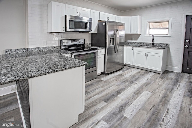 kitchen featuring light wood-style flooring, a peninsula, stainless steel appliances, dark stone counters, and a sink
