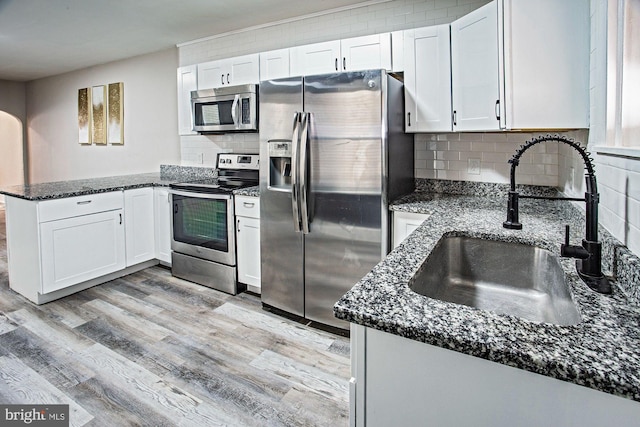kitchen featuring a sink, a peninsula, stainless steel appliances, white cabinets, and light wood-style floors