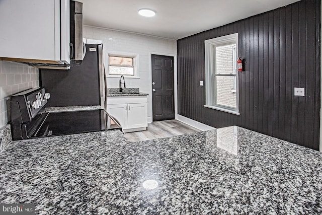 kitchen with dark stone counters, white cabinets, a sink, and backsplash