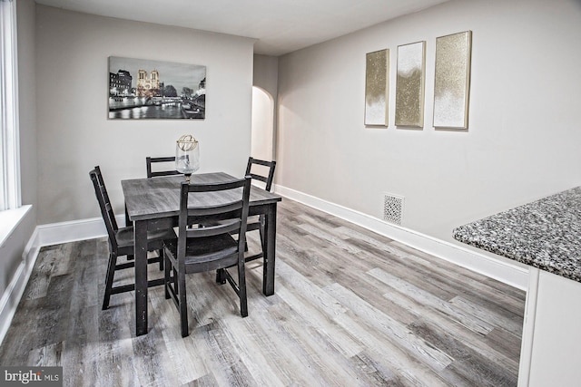 dining space featuring visible vents, arched walkways, baseboards, and wood finished floors