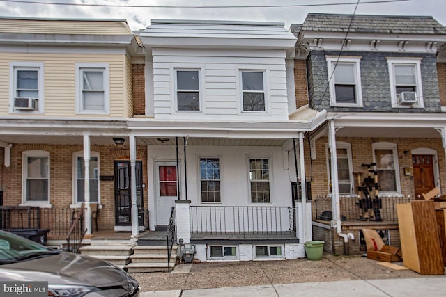 townhome / multi-family property with cooling unit, covered porch, mansard roof, and brick siding