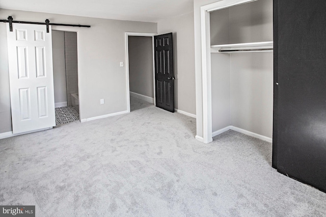 unfurnished bedroom featuring a closet, a barn door, baseboards, and carpet