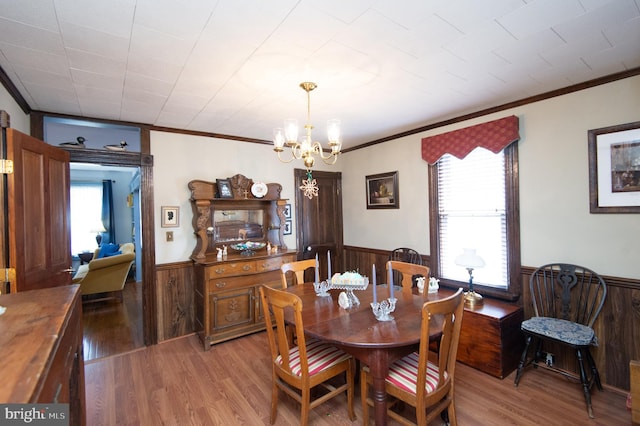 dining room with a wainscoted wall, light wood-style floors, wood walls, and a chandelier