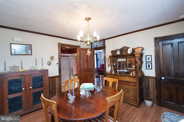 dining room featuring crown molding, wood walls, wainscoting, a notable chandelier, and wood finished floors