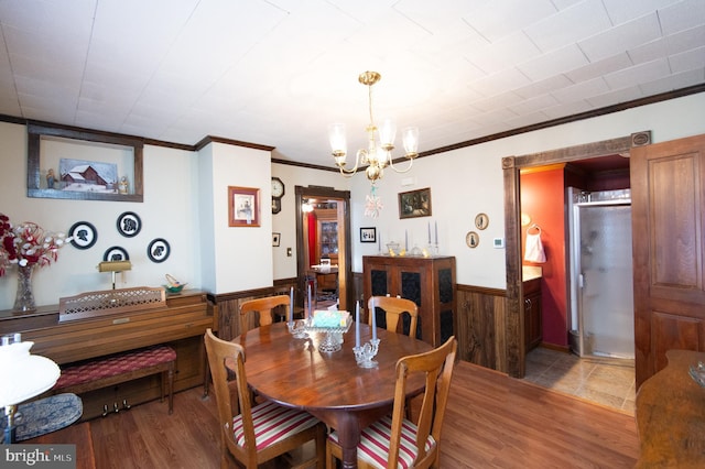 dining room featuring crown molding, a chandelier, wooden walls, wainscoting, and light wood-style flooring