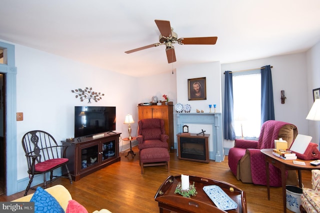 living area featuring baseboards, wood finished floors, a glass covered fireplace, and a ceiling fan