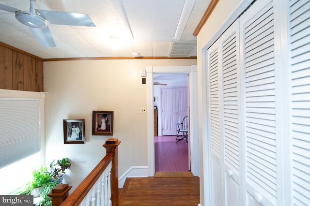 corridor featuring an upstairs landing, wood finished floors, baseboards, visible vents, and ornamental molding