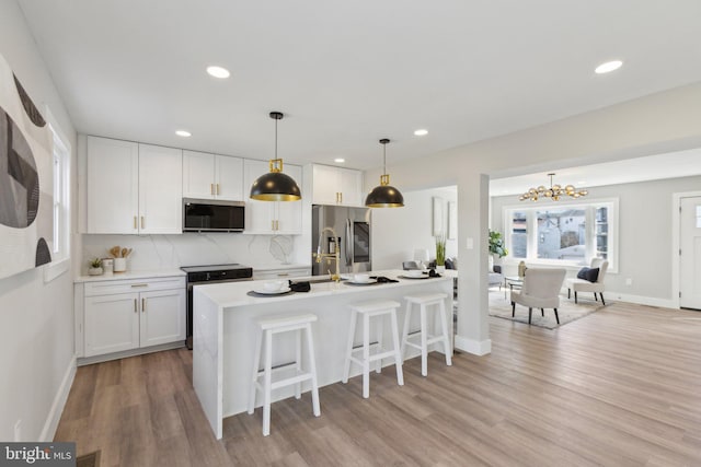 kitchen featuring light wood finished floors, tasteful backsplash, appliances with stainless steel finishes, white cabinetry, and a breakfast bar area