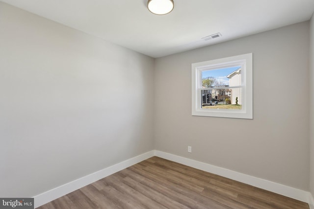 empty room featuring baseboards, visible vents, and wood finished floors