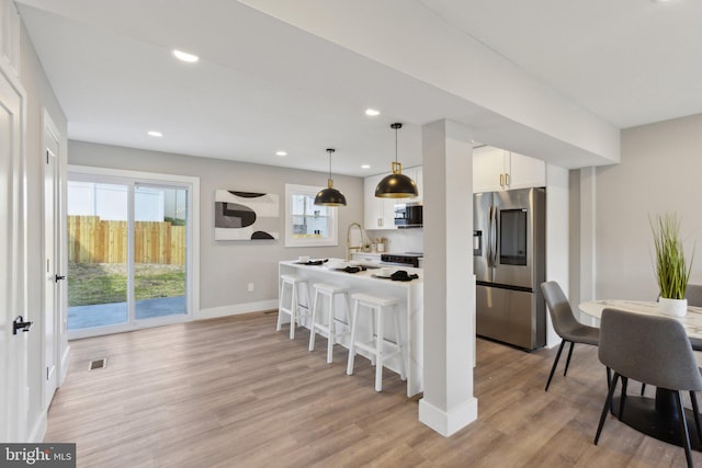 kitchen featuring white cabinets, visible vents, light wood-style flooring, appliances with stainless steel finishes, and a kitchen breakfast bar