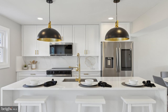 kitchen featuring decorative backsplash, light countertops, a center island with sink, appliances with stainless steel finishes, and white cabinetry