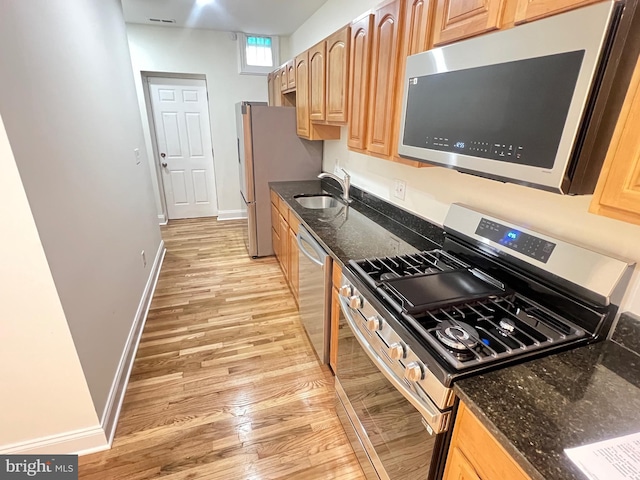 kitchen featuring dark stone countertops, a sink, light wood-type flooring, and appliances with stainless steel finishes