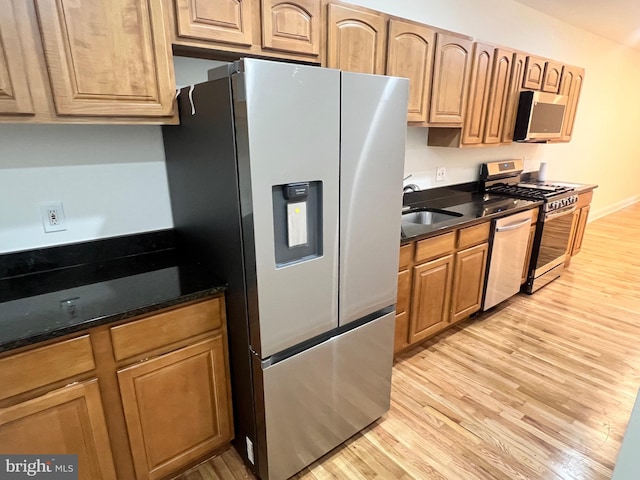 kitchen featuring a sink, stainless steel appliances, dark stone countertops, and light wood-type flooring
