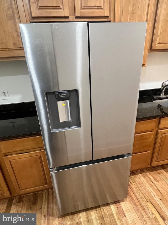 interior details with brown cabinetry, light wood-style floors, dark stone countertops, and stainless steel refrigerator with ice dispenser