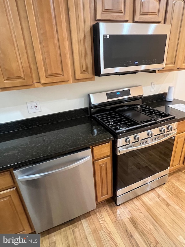 kitchen featuring light wood finished floors, dark stone counters, and stainless steel appliances