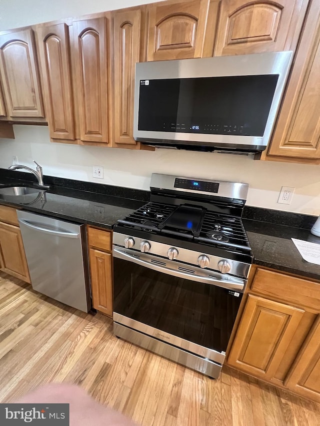 kitchen featuring a sink, appliances with stainless steel finishes, dark stone countertops, and light wood-type flooring