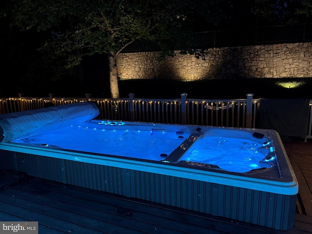 pool at night featuring a hot tub and a deck