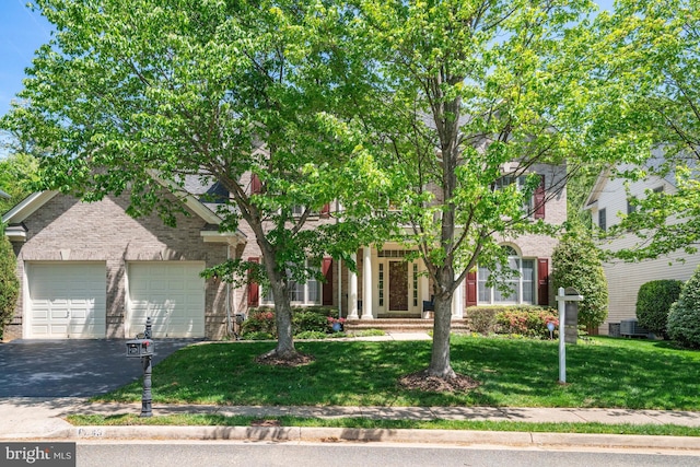 obstructed view of property featuring a front yard, brick siding, an attached garage, central air condition unit, and driveway