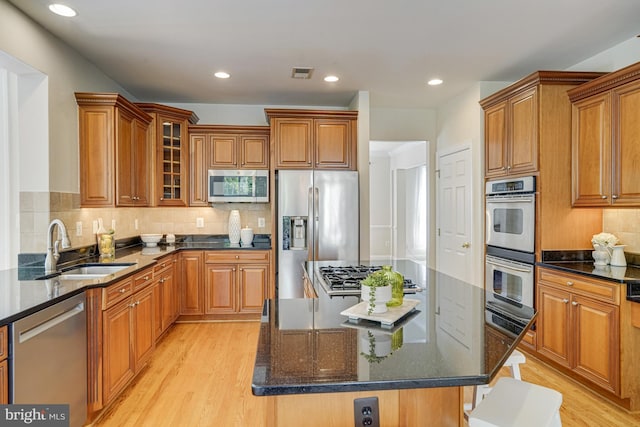 kitchen with a sink, brown cabinetry, a center island, stainless steel appliances, and light wood-type flooring