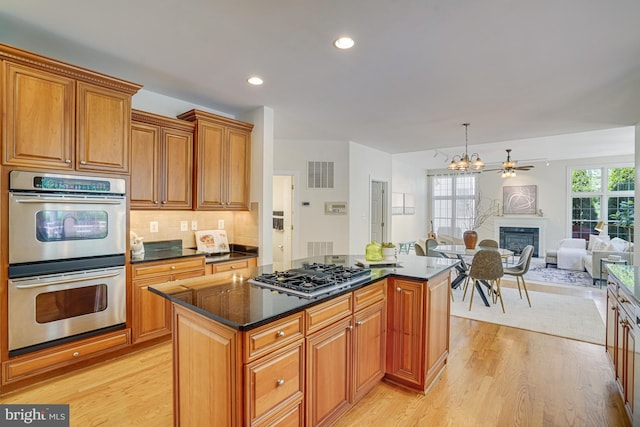 kitchen with appliances with stainless steel finishes, a center island, brown cabinets, light wood finished floors, and a glass covered fireplace
