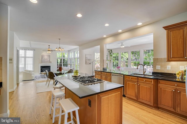 kitchen with a sink, brown cabinetry, ceiling fan with notable chandelier, and light wood finished floors