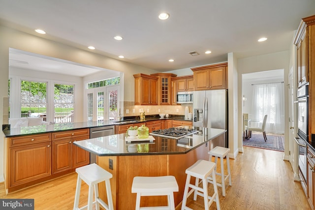 kitchen featuring brown cabinetry, appliances with stainless steel finishes, a breakfast bar area, and light wood-type flooring