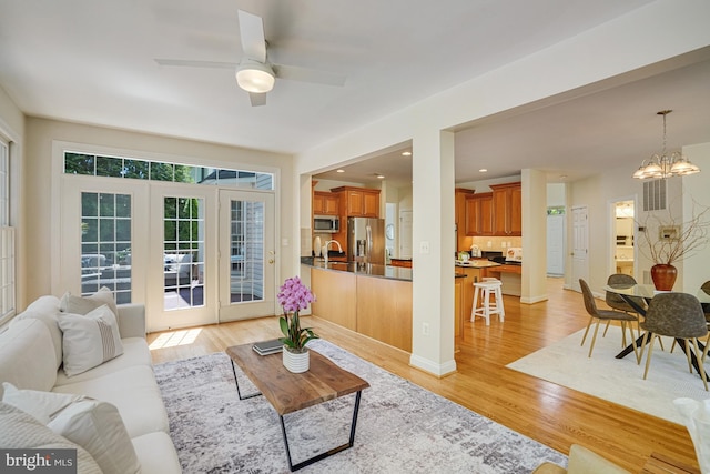 living area featuring french doors, ceiling fan with notable chandelier, and light wood-type flooring