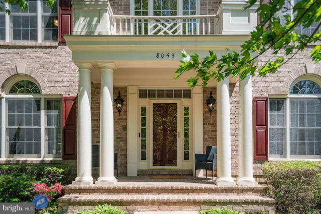 doorway to property with brick siding, a balcony, and covered porch