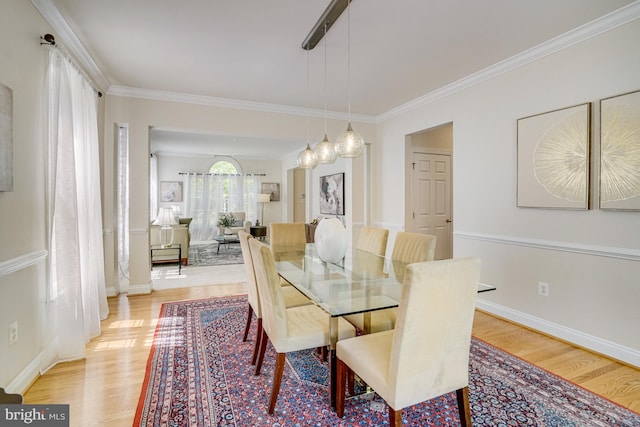 dining area featuring light wood-style floors, ornamental molding, and baseboards