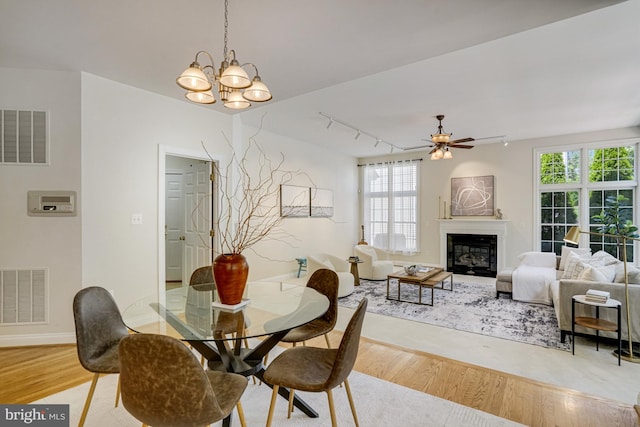 dining area featuring visible vents, light wood-style floors, a glass covered fireplace, and track lighting