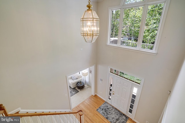 entrance foyer with baseboards, a towering ceiling, wood finished floors, and a notable chandelier
