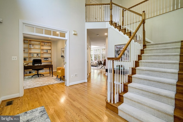 stairway with baseboards, visible vents, wood finished floors, and a towering ceiling