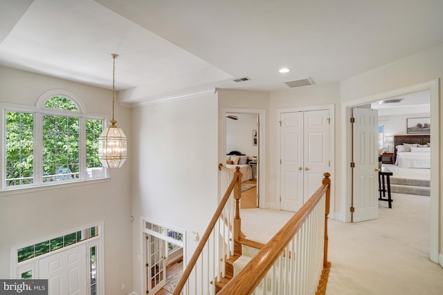 hallway with light colored carpet, an upstairs landing, an inviting chandelier, and visible vents