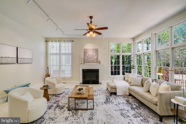 living room featuring track lighting, a fireplace with flush hearth, ceiling fan, and a healthy amount of sunlight