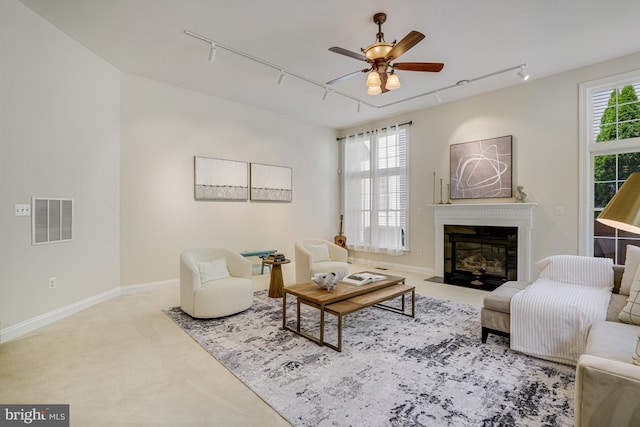 living room with a fireplace with flush hearth, track lighting, a ceiling fan, and visible vents