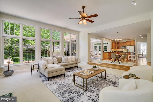 living room featuring baseboards, recessed lighting, ceiling fan with notable chandelier, and light colored carpet