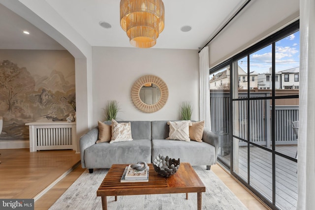 living room with light wood-style floors, baseboards, arched walkways, and radiator