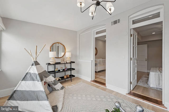 living area featuring baseboards, visible vents, wood finished floors, and a notable chandelier