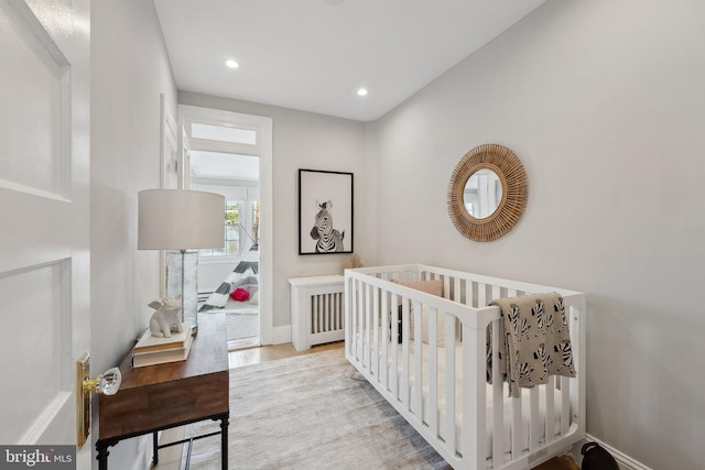 bedroom featuring light wood-style floors, recessed lighting, baseboards, and a crib