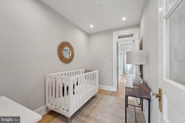 bedroom with baseboards, recessed lighting, wood finished floors, and a nursery area