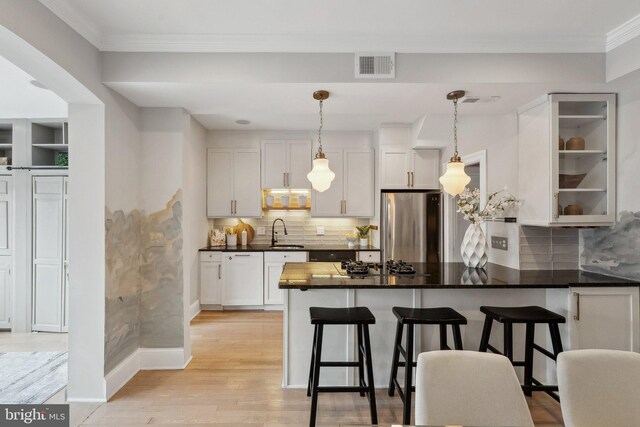 kitchen with a sink, dark countertops, visible vents, freestanding refrigerator, and a peninsula