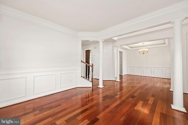 spare room with an inviting chandelier, ornamental molding, decorative columns, a decorative wall, and hardwood / wood-style flooring