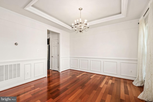 spare room with a raised ceiling, wainscoting, a chandelier, and visible vents