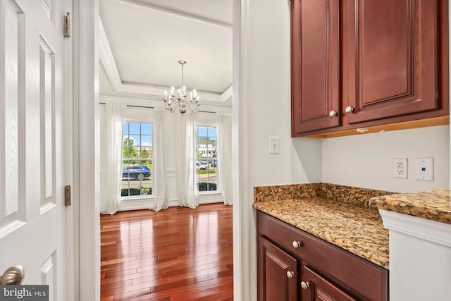 interior space with crown molding, a raised ceiling, wood-type flooring, a chandelier, and decorative light fixtures